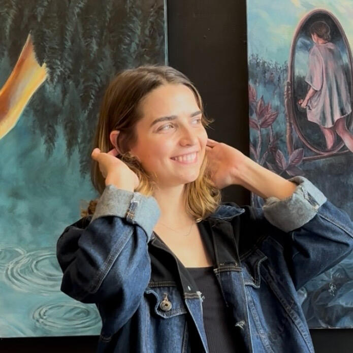 Laura Stockdale smiling for a photo in front of a painting, holding a paintbrush.